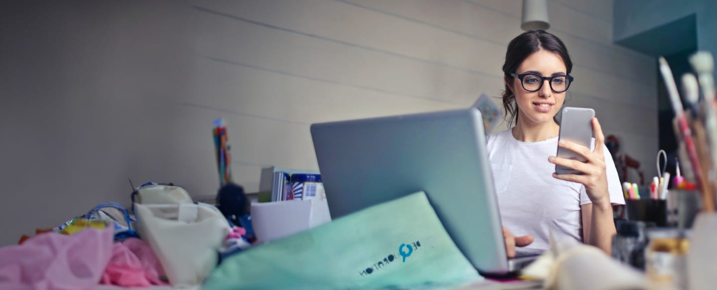 Frau am Laptop mit Handy in der Hand